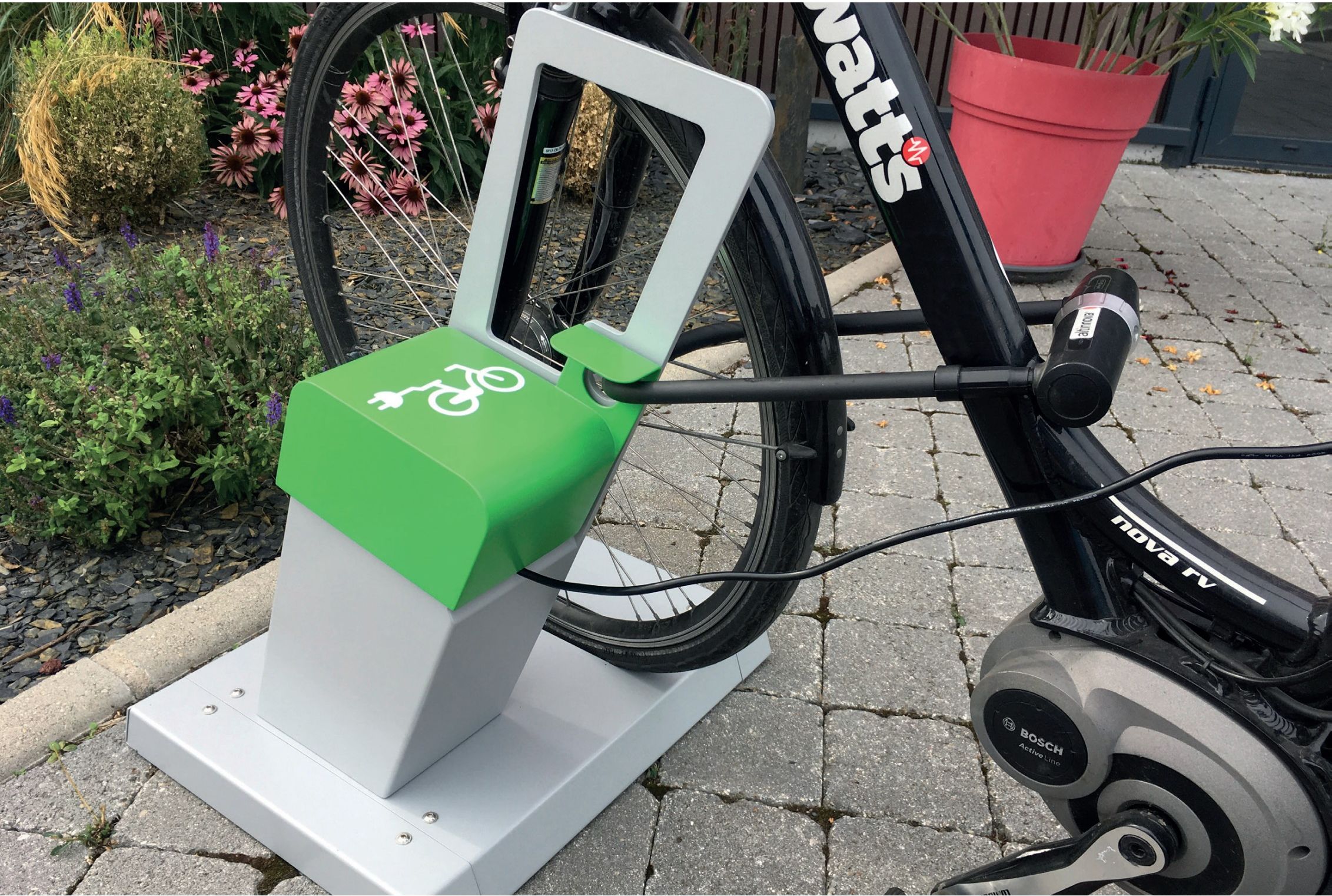 Colonnina di ricarica ALTAO® Parco e-bike con e-bike collegata e vano verde per il caricabatterie